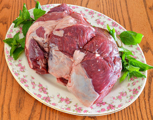 raw lamb leg roast on floral plate with garnishes