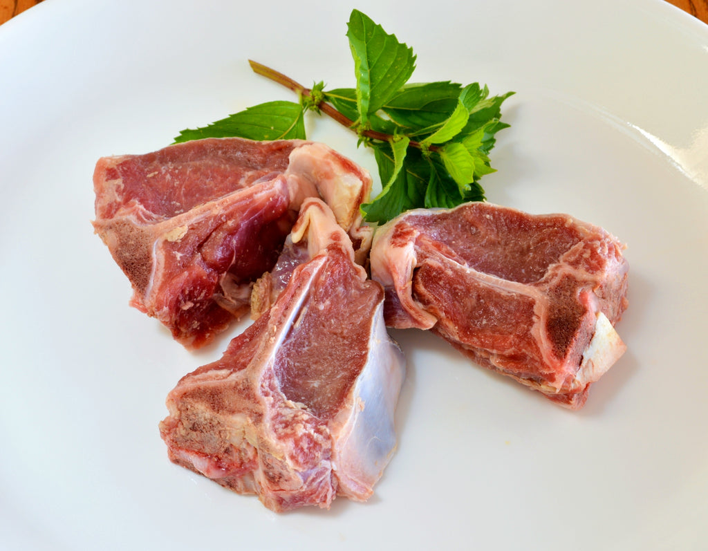 raw lamb loin chops on white plate with garnishes